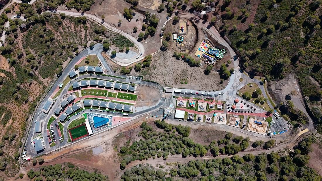 Aerial view of a hillside resort with a pool and sports pitch